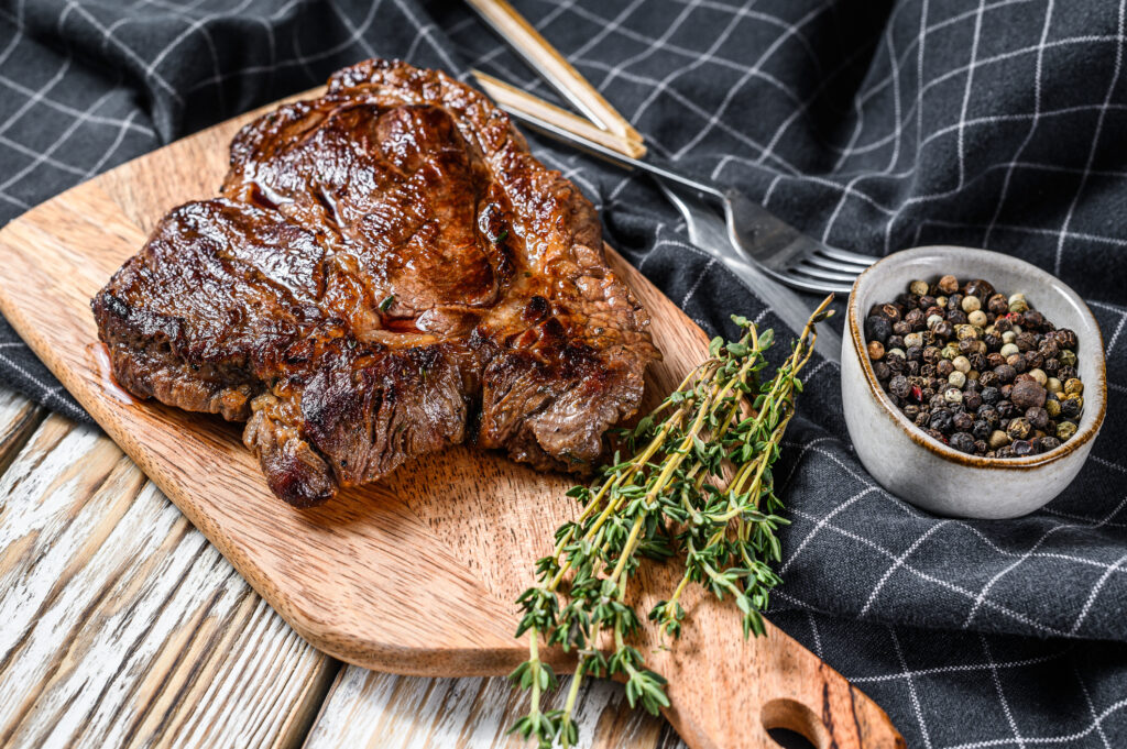 Chuck roast grilled on a checked tablecloth and wood cutting board with a bowl of peppercorns to the side
