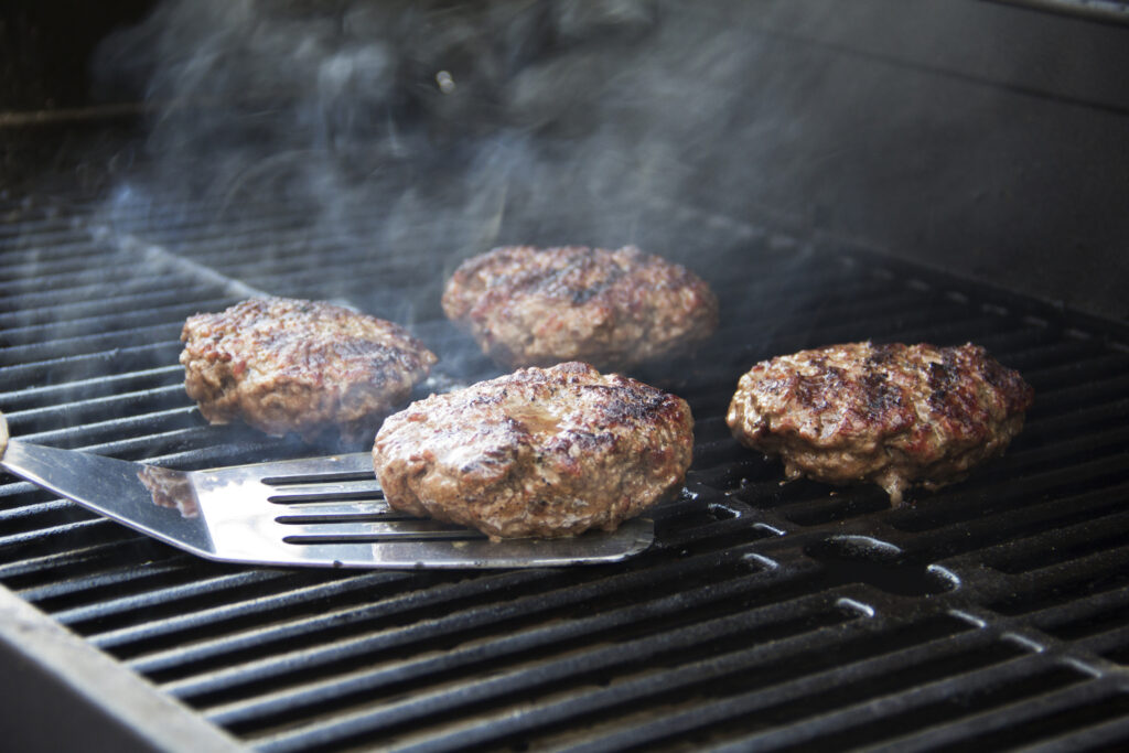 Perfectly grilled burgers coming off the grill with a metal spatula. Griller's Gold Blog