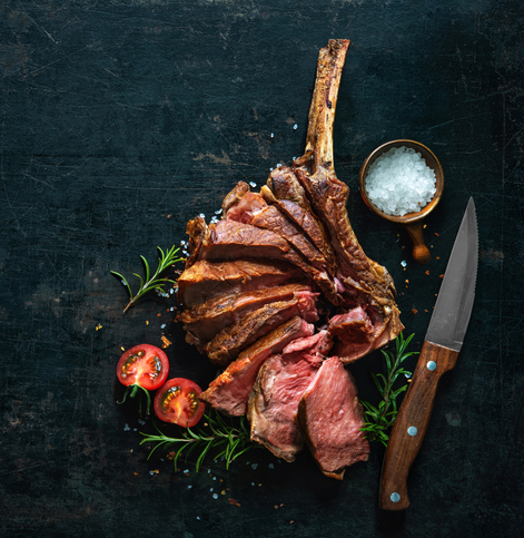 sliced tomahawk steak with a knife, sliced tomato and small bowl of salt