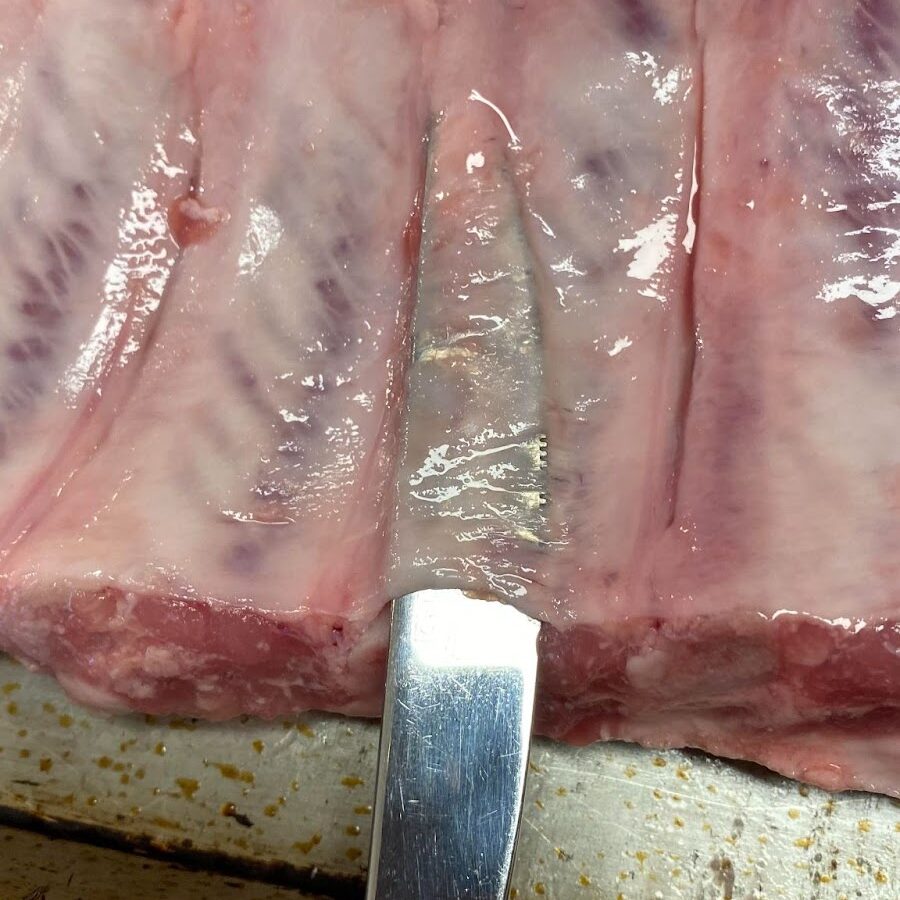 Ribs with a butter knife showing where to insert the butter knife to remove the membrane