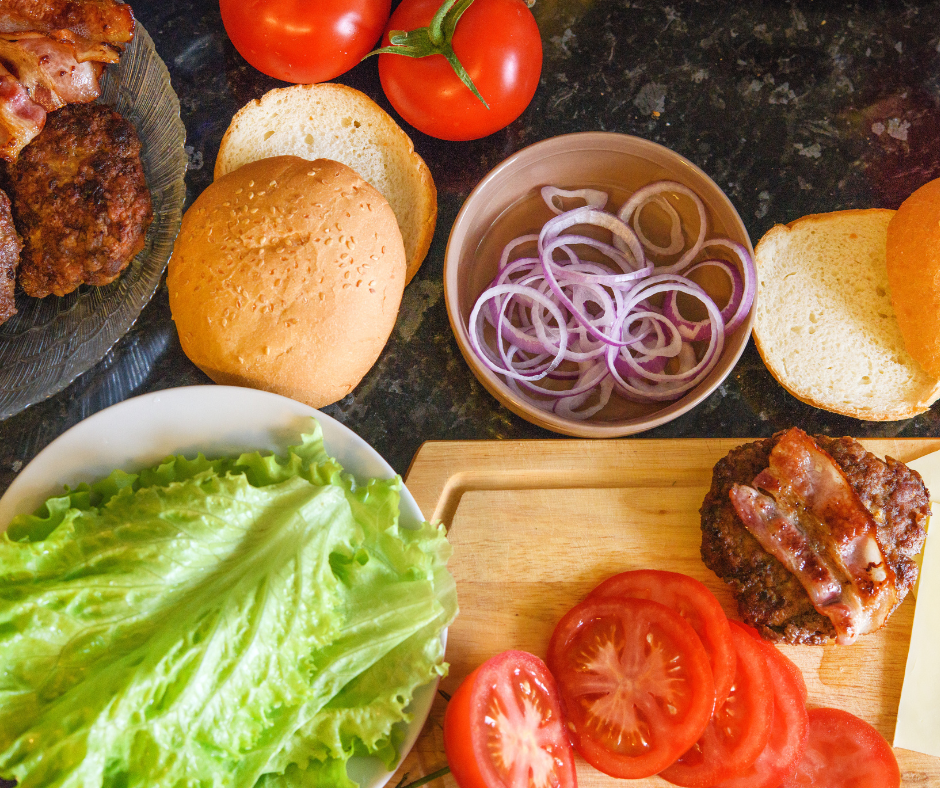 an assortment of toppings for a burger bar - onions, tomatoes, lettuce and bacon