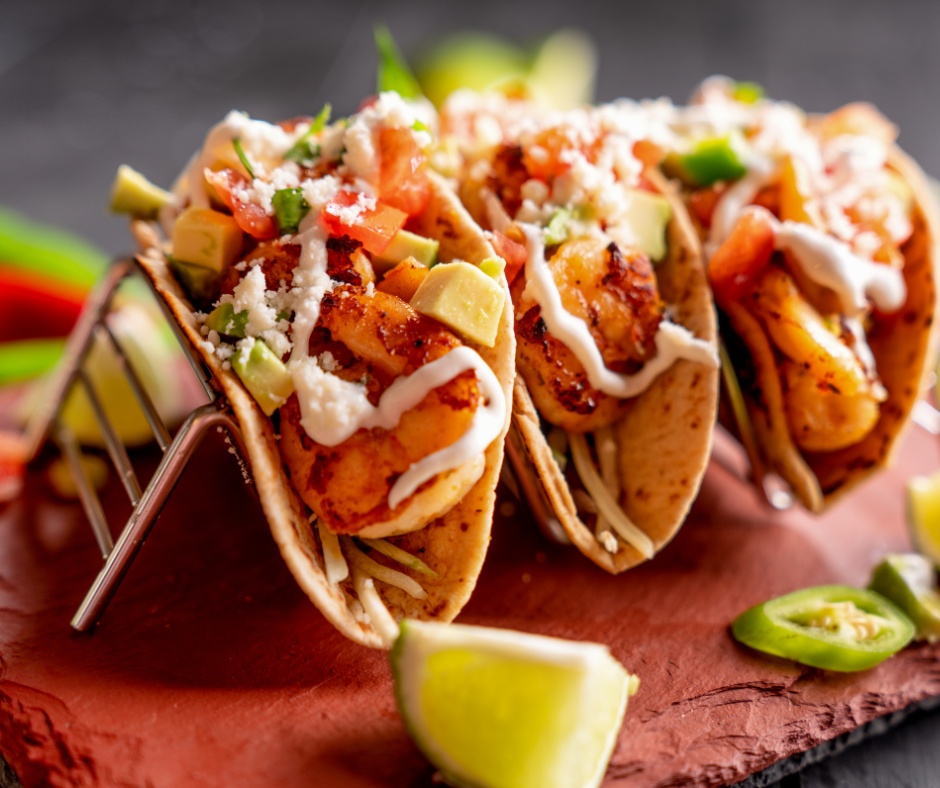 three tacos in a metal taco holder with fish tacos inside. Mango slaw and other toppings