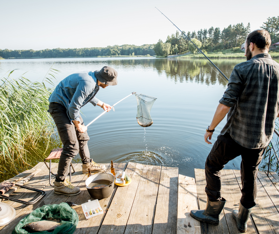 two men on a wooden dock with a fish in a net on a lake