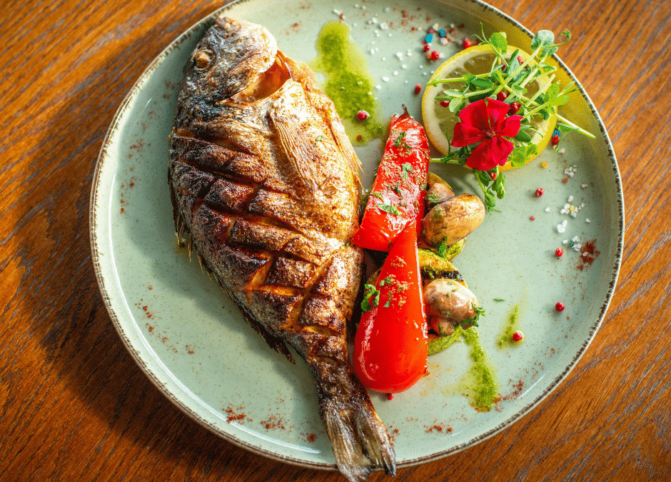 A full fish on a blue plate with peppers and a tomato