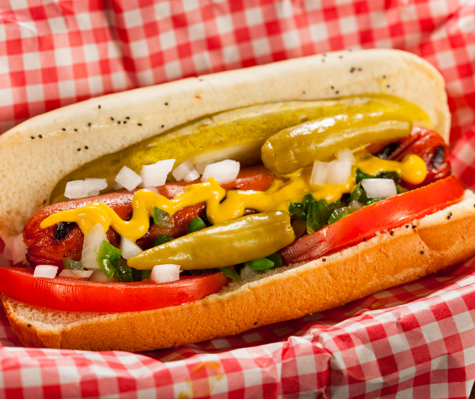 a Chicago hot dog in a red and white checkered basket. It is in a bun with mustard, peppers, pickles, onions and green relish