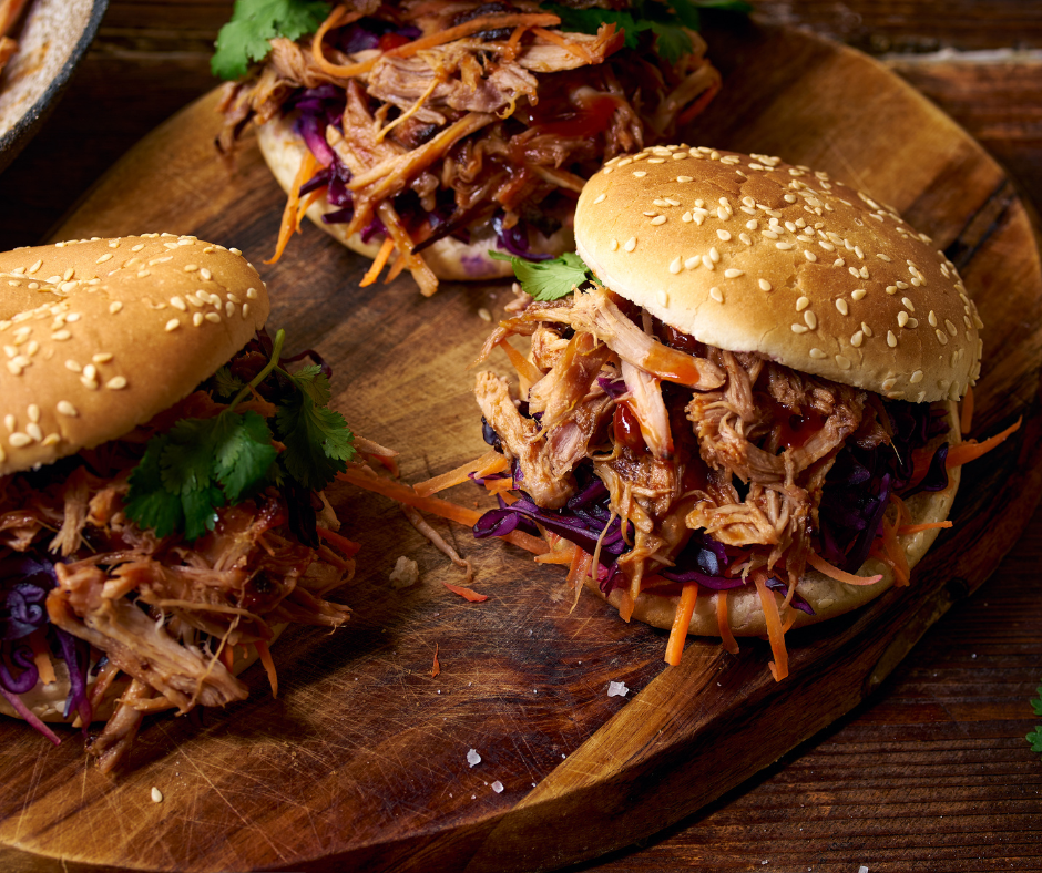 3 pulled pork sandwiches on a wood cutting board. Coleslaw and cilantro as garnish