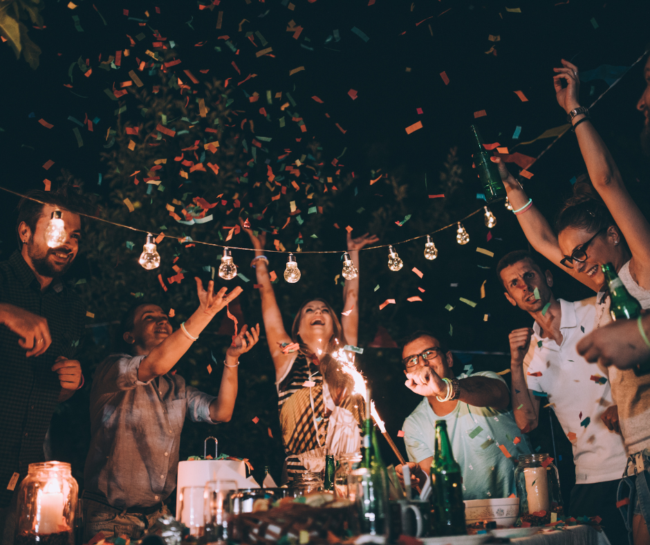A group of people throwing confetti into the air at some sort of a party outside.