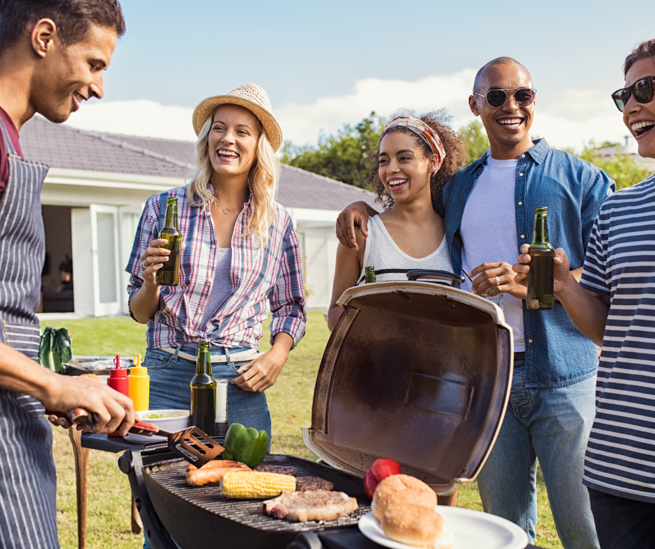 A group of 25-30 something people standing around a grill with corn, pepper, hot dogs and steak.
A man with fark hair at the grill, a woman with blonde hair and a hat standing next to a woman with dark skin wearing a white tank top,, next to a man with dark skin wearing a white tshirt and jean shirt, next to a man wearing shades and a blue and white striped shirt. All American backyard grilling at its finest