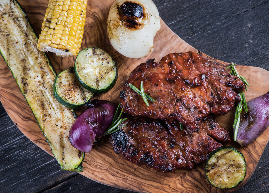 grilled corn, onions and zucchini on a wood board with grilled pork and herbs on top